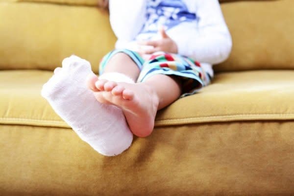 Copil cu imobilizare gipsată la picior, stând liniștit pe canapea