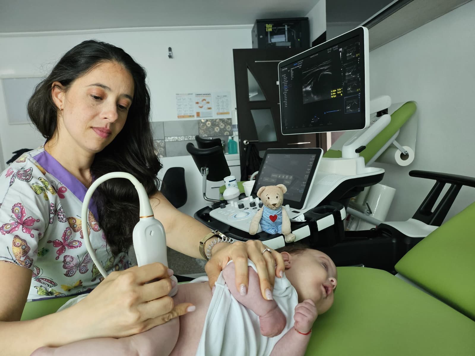 Dr. Yasmin Al-Hiary efectuând o ecografie de șold unui bebeluș, cu imaginea articulației pe ecranul ecografului
